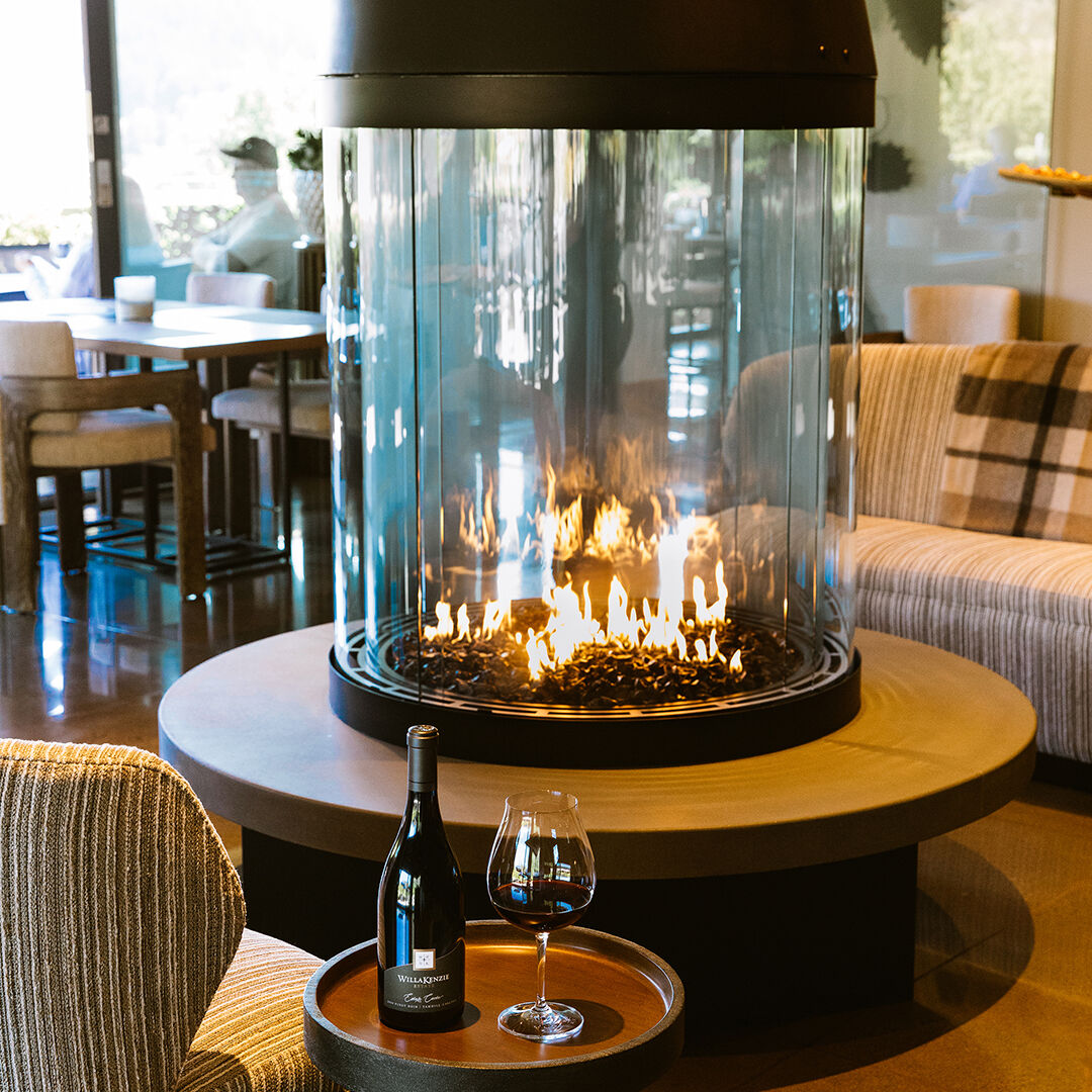 A shot of a WillaKenzie Estate tasting room with bottle and glass in front of the fire.